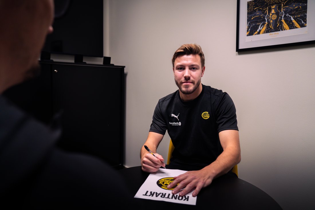 Fredrik André Bjørkan signerer sin nye kontrakt med Bodø/Glimt på kontoret til sportslig leder Håvard Sakariassen på Aspmyra og ser i kameraet