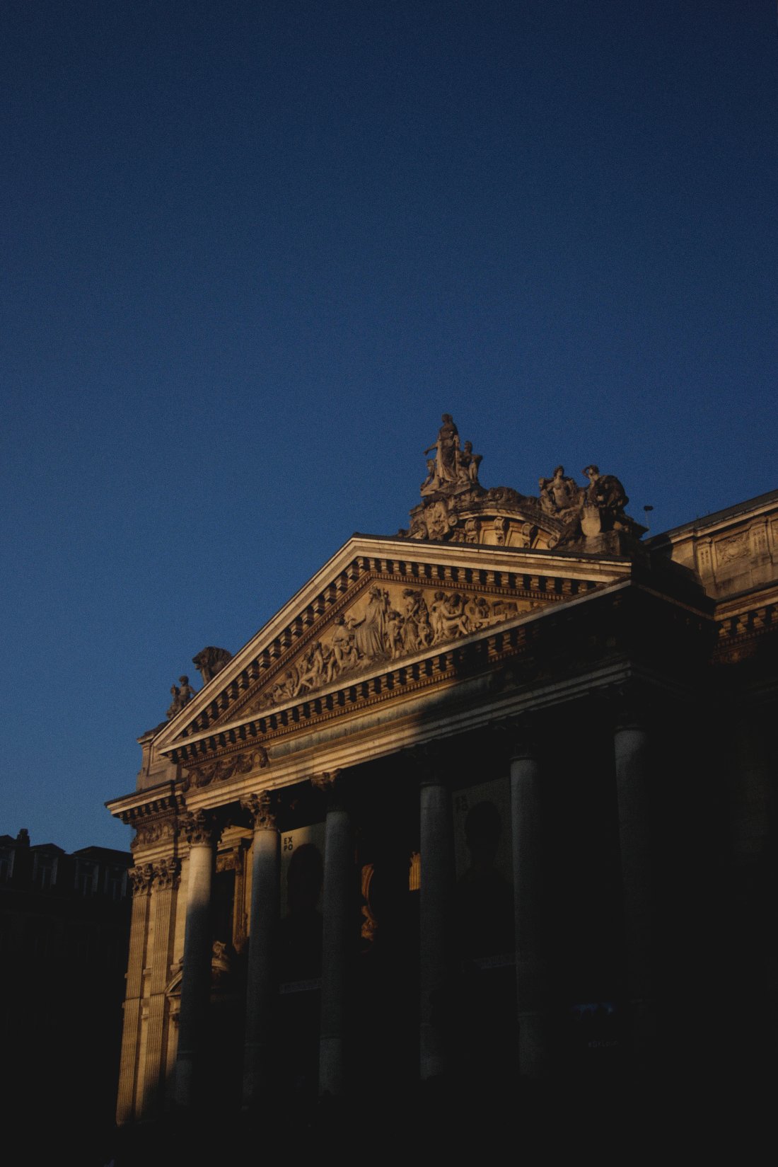 Bilde av en bygning i Brussel som ligger delvis i skyggen og delvis i solen tatt fra bakken mot en mørk og dyp blå himmel