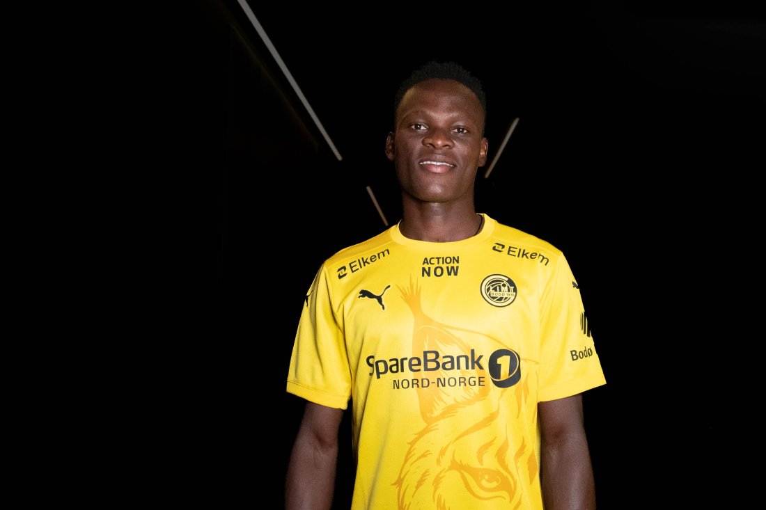 Gift Sunday har signert for Bodø/Glimt og poserer i den gule Glimt-drakta i et mørkt rom der bare han er opplyst