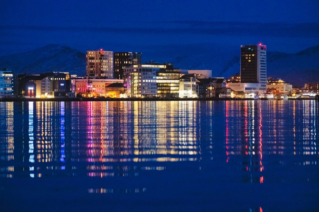 Utsikt over Bodø by i mørk vinterlys. Byen speiler seg i havet med fjellene i bakgrunnen