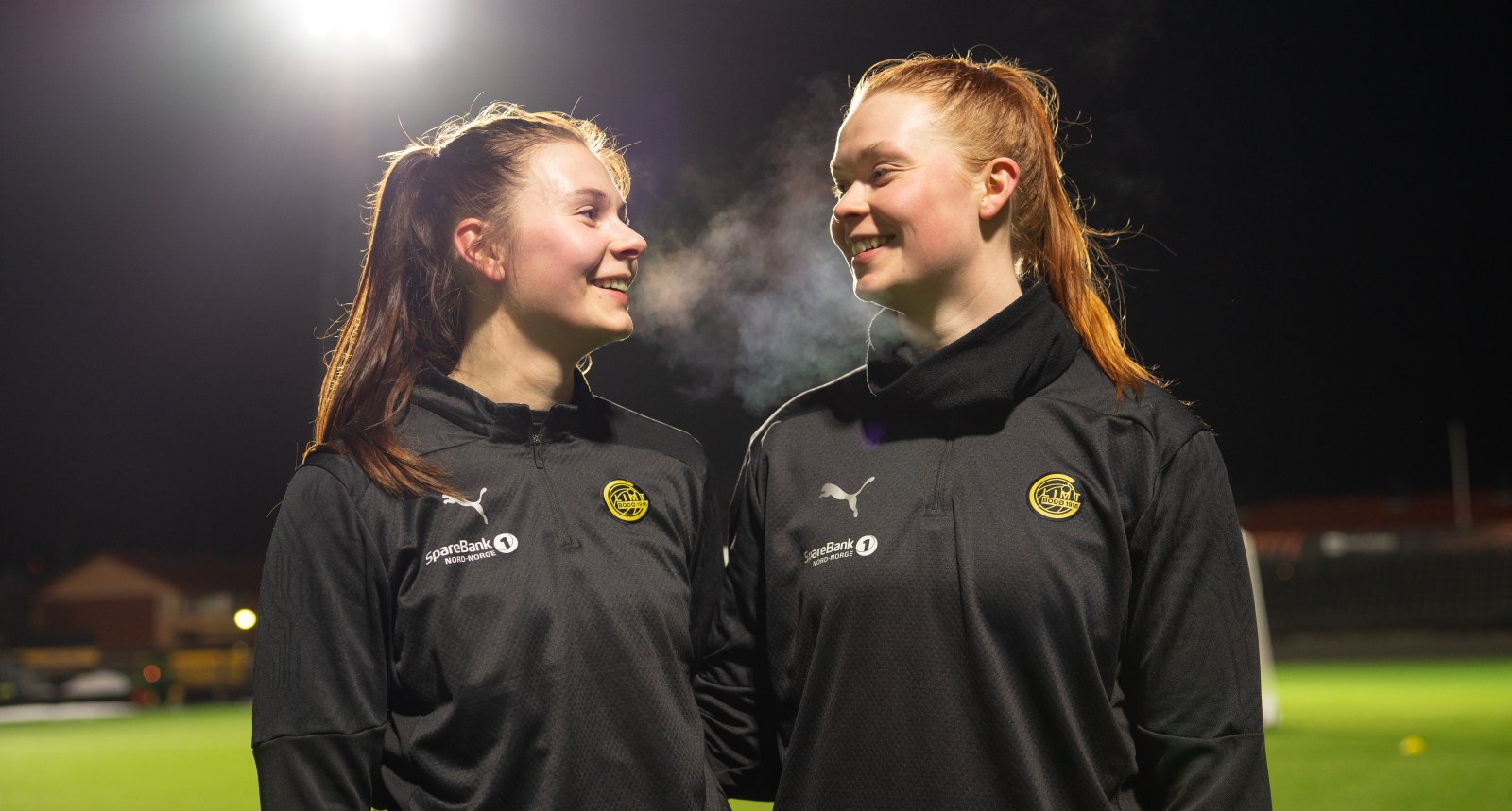 Bildet viser Anna og Gerd som smiler til hverandre under årets første trening på Aspmyra stadion.